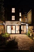 Courtyard with paved area at night and view into modern extension with illuminated interior