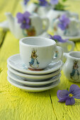 Crockery with Peter Rabbit motif and violas on yellow-painted wooden table