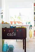 Sideboard dekoriert mit Wimpelgirlande und 'café'-Schriftzug, im Hintergrund Grünpflanzen vor Fenster in Mädchenzimmer