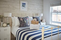 Doppelbett mit weißem Metallgestell und weiss-blau gestreifter Tagesdecke in ländlichem Schlafzimmer