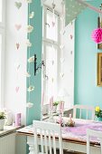 White-painted chairs around vintage dining table next to window behind romantic garlands and fairy lights