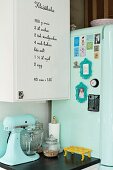 Mixer on kitchen cabinet next to mint-green retro fridge decorated with magnets