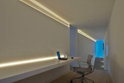 Modern office chair at long desk with indirect lighting in minimalist study with staircase in background