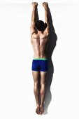 Muscular young man wearing blue shorts hanging from white wall