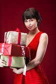Dunkelhaarige Frau in rotem, ärmellosem Kleid hält Geschenkpakete