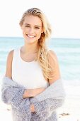 Junge blonde Frau in weißem Top und lila Strickjacke am Strand