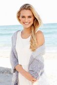 Young blonde woman wearing white dress and lilac cardigan on beach