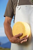 A cheesemaker with a wheel of cheese made from silage-free milk