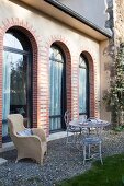 Delicate metal furniture and wicker chair on gravel terrace outside elegant country house with arched windows