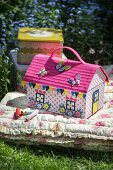 Colourful, house-shaped sewing box on floral floor cushion in garden