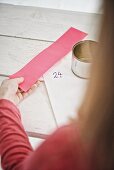 Tin can, sticker and pink paper in girl's hand for making DIY Advent calendar