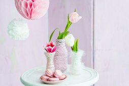 Tulips in vases wrapped in cord next to plate of pink macarons