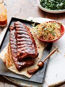 Marinated spare ribs on a baking tray with a bowl of coleslaw