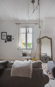 Folded blanket on sofa and mirror leaning against wall next to lattice window in vintage living room