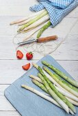 Green and white asparagus wrapped in tea towels with a peeler, strawberries and asparagus peelings