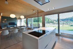 Kücheninsel in Designerstil vor Glaswand zum Essbereich und Fensterfront mit Jalousie