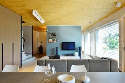 Blick vom Essbereich in offenen Designer-Wohnbereich mit Fernseher an pastellblauer Wand
