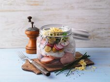A layered sausage salad with radishes in a jar