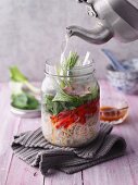 Sweet-and-sour soup with ham and bok choy in a jar being filled with water