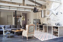 Antique armchair and chair around coffee table, dark grey sofa and kitchen counter in open-plan interior