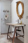 Rustikaler Waschtisch vor Spiegel mit Goldrahmen an weiss gefliester Wand