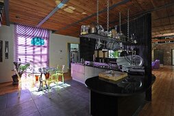 Essplatz mit transparenten Kunststoffstühlen und lilafarbener Jalousie in offener Küche einer Loftwohnung mit Industriecharme