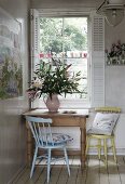 Kitchen chairs at rustic wooden table in corner below window with open white shutters