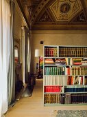 High painted ceiling and bookcase used as partition in living room of palazzo