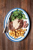 Grilled rib-eye steak with fried potatoes, lettuce and pepper sauce