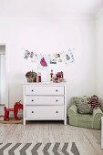 Kinderzimmer mit weisser Schubladenkommode, Schaukeltier und grünem Kindersessel, Wanddekoration mit Zeichnungen und Fotos an Wäscheleine