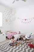 Bright girl's room with fabric pennant chain and playing girl on carpet