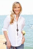 A young blonde woman by the sea wearing a white blouse and jeans
