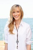 A young blonde woman by the sea wearing a white blouse and jeans