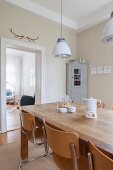 Cantilever chairs around wooden table below retro pendant lamps; corner cupboard next to open doorway in background