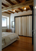 Doppelbett und begehbarer Kleiderschrank hinter Vorhang im Schlafzimmer mit rustikaler Holzbalkendecke