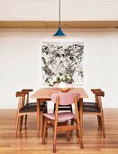 Wooden chairs with leather-covered upholstery around a table with retro flair in front of a wall with a modern image