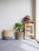 Vitrinenschränkchen mit gestapelten Hüten, Zimmerpflanze in Korbübertopf und Korbtasche auf Teppichboden