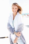 A blonde woman on a beach wearing a white blouse and a purple cardigan