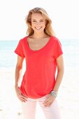 A blonde woman on a beach wearing a red top and pink trousers