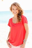 A blonde woman on a beach wearing a red top and pink trousers