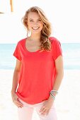 Blonde Frau in rotem Shirt und rosa Hose am Strand