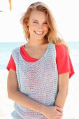 A blonde woman on a beach wearing a red top and a crocheted top