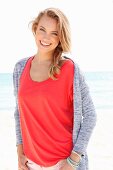 A blonde woman on a beach wearing a red top and a cardigan