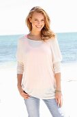 A blonde woman on a beach wearing a top, a thin, long-sleeved top and jeans