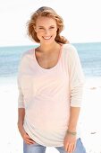 Blonde Frau in Top, dünnem Langarmshirt und Jeans am Strand