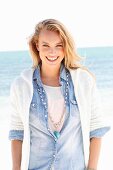 A young woman on a beach wearing a denim shirt and a cardigan