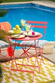 Red metal table and chairs on rug in colourful seating area next to pool