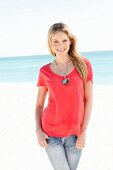 A young woman on a beach wearing a red top and jeans