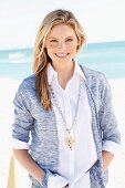 A young woman on a beach wearing a white blouse and a cardigan