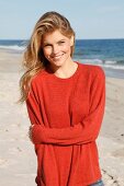 A young woman on a beach wearing a rust-red jumper and jeans